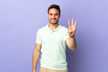 Young handsome man isolated on purple background happy and counting three with fingers