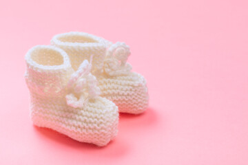 knitted baby booties on pastel pink background.