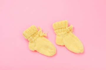 knitted baby booties on pastel pink background.