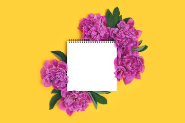 Top view of square notepad mockup and frame made of peony flowers on a yellow background. Spring concept.