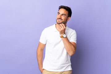 Young handsome man isolated on purple background looking up while smiling