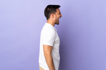 Young handsome man isolated on purple background laughing in lateral position