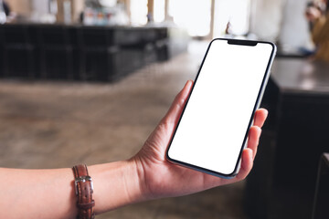 Mockup image of a woman holding mobile phone with blank white desktop screen in cafe