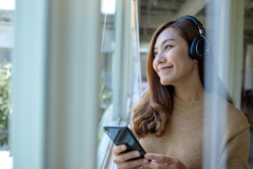A beautiful young asian woman with headphone enjoy listening to music on smart phone