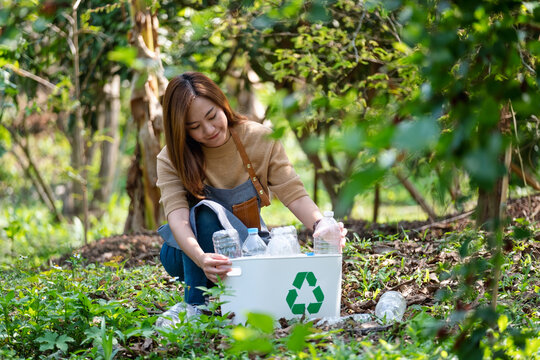 A beautiful young asian woman collecting and putting plastic bottles into a recycle bin in the outdoors