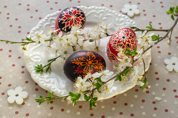 Homemade handmade painted Easter eggs on white plate on spotted tablecloth decorated with...