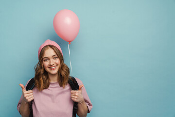 Young white student girl showing thumb up while posing with balloon