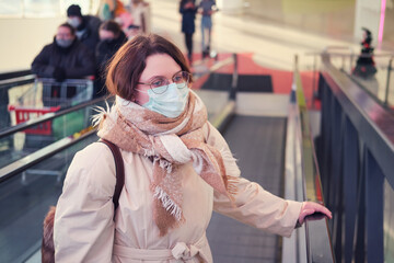 Face adult woman in a medical mask with red hair on the escalator of a shopping mall