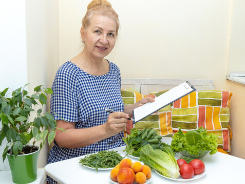 Senior woman nutritionist working in home office, writing diet plan using fruits and vegetables.