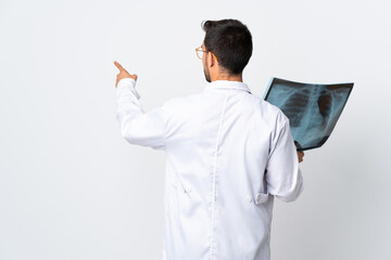 Young doctor man holding a radiography isolated on white background pointing back with the index finger