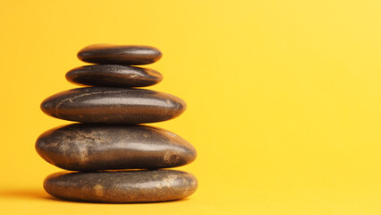Fototapeta na wymiar Five stacked dark massage stones on yellow
