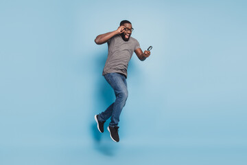 Young afro man jump look magnifying glass isolated over blue background