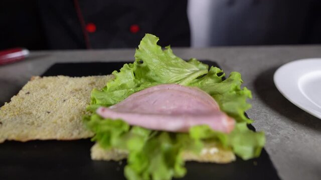 the process of making focaccia with turkey ham in the kitchen. Chef's hands lay meat on a sandwich with green lettuce.