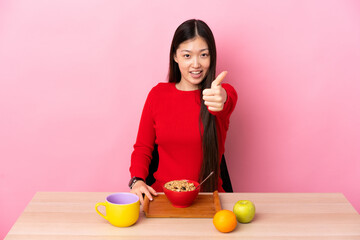 Young Chinese girl  having breakfast in a table with thumbs up because something good has happened