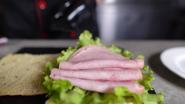 the process of making focaccia with turkey ham in the kitchen. Chef's hands lay meat on a sandwich with green lettuce.