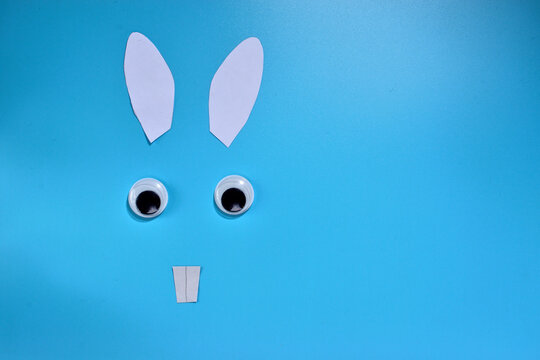 paper ears with teeth and plastic eyes of a christmas bunny on a blue background with copy space