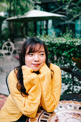 Close up of young pretty Asian woman in blue yellow sweater with garden background.