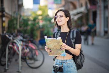  Female tourist searching for city destination on map outdoors.  Woman standing on street with map in hands.