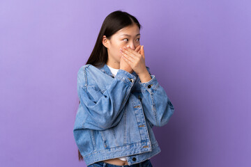 Young Chinese girl over isolated purple background covering mouth and looking to the side