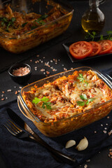 Tasty hot lasagna served on black background. Italian cuisine, menu, recipe. Homemade meat lasagna. Close up, side view.