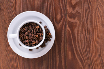 white cup, saucer and coffee beans on a wooden background