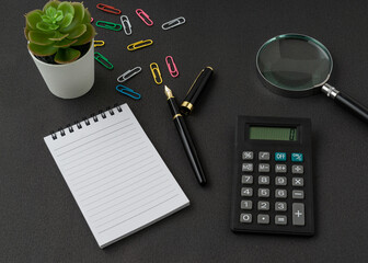 A notebook, calculator, magnifying glass and pen on black background with a copy space. Business and finance concept.