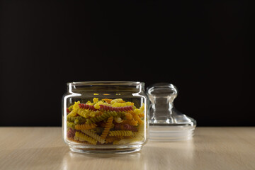 Colored pasta in a glass jar on a black background.