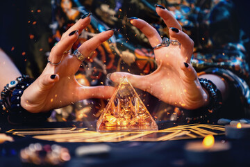 A witch conjures a magic glass pyramid. Hands close-up. Sparks flare up near the pyramid. The concept of witchcraft and divination - obrazy, fototapety, plakaty