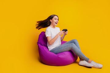 Profile photo of lady sit beanbag play videogame hold controller wear white t-shirt posing on yellow background © Tetiana