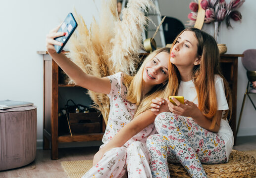Two teenage sisters take a selfie on the phone. Happy nice girls make a photo on a smartphone camera for social networks. Young women have activities for pleasure and fun.