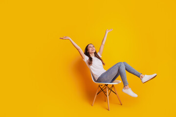 Photo of dreamy inspired lady sit chair raise arms look up empty space wear white t-shirt posing on yellow background