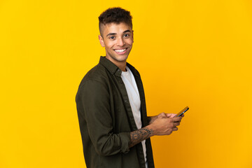 Young brazilian man isolated on yellow background sending a message or email with the mobile