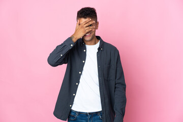 Young Brazilian man isolated on pink background covering eyes by hands and smiling