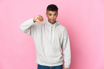 Young Brazilian man isolated on pink background showing thumb down with negative expression