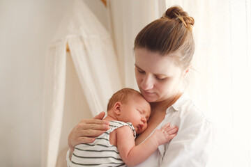 Cute calm caucasian mom with her newborn baby. Mother in a white shirt hugs and gently strokes the...