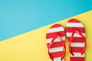 Top view photo of striped red and white flip-flops on bicolor yellow and blue background with copyspace