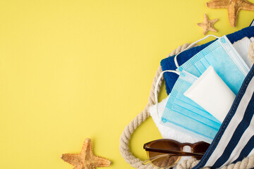 Top view photo of starfishes beach bag with towels white tube cream sunglasses and medical masks on isolated yellow background with copyspace