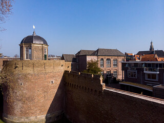 Closeup aerial view of historic Bourgonje stronghold tower and city wall with historic city center of Zutphen, The Netherlands, in the background against a blue sky