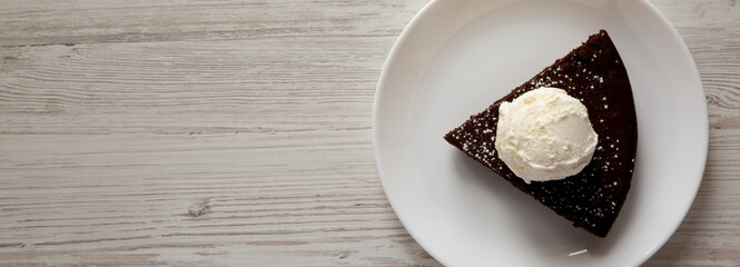 Homemade Chocolate Cake with Ice Cream on a white plate on a white wooden surface, top view. Flat lay, overhead, from above. Copy space.