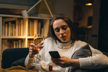 depressed woman drinking wine and crying, sitting on sofa at her home. evening scene