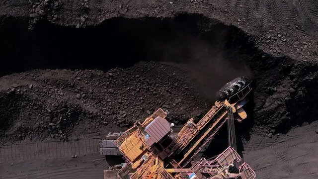 View from above. Open pit coal mining. Large mining equipment picks up coal from the warehouse with a bucket.
