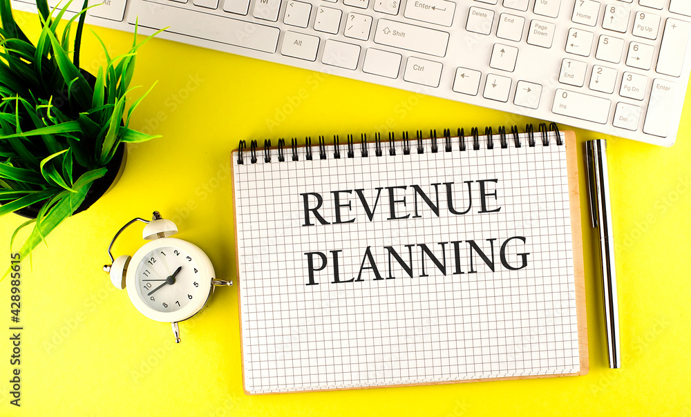 Aufkleber revenue planning text on notebook with keyboard , pen and alarm clock on the yellow background