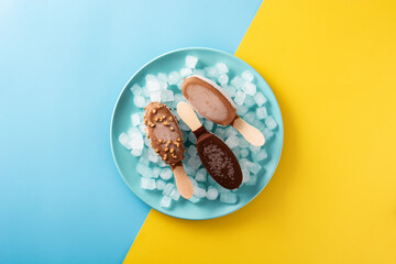 Chocolate popsicles and crushed ice on blue plate on yellow and blue background
