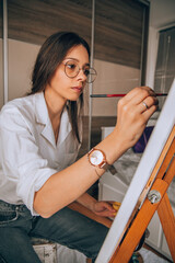 Beautiful talented female artist painting at her home.