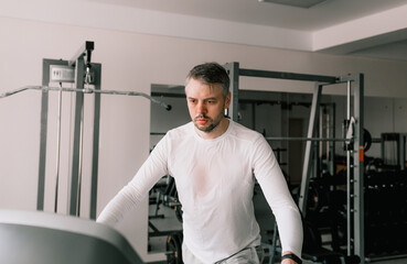 Fototapeta na wymiar a tired man in a sweat-soaked T-shirt runs on a treadmill in a sports club. cardio workout