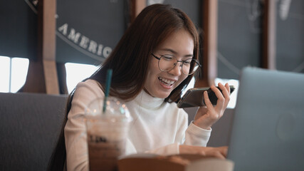 Fototapeta na wymiar Asian woman talking on the phone with customer happily enjoying working time outside office at coffee shop.