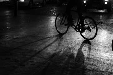Fototapeta na wymiar Silhouette and shadow cast by a cyclist and his bicycle illuminated by car lights