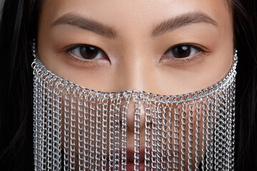 The face of a beautiful Asian girl with expressive eyes in a decorative mask made of chains,...