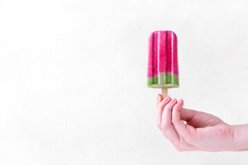 Two-colored popsicle held in woman hand against the white background. Copy space. Summertime dessert