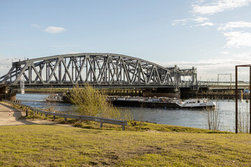 Steel train and traffic draw bridge over the river IJssel with a cargo ship passing by near the Dutch Hanseatic city of Zutphen, The Netherlands, seen from the floodplains against a blue sky